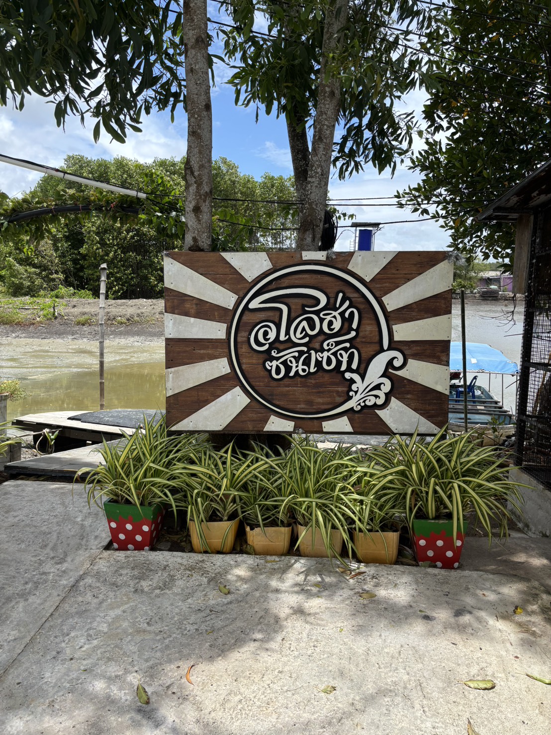 ป้าย Aloha Sunset ริมน้ำท่ามกลางต้นไม้